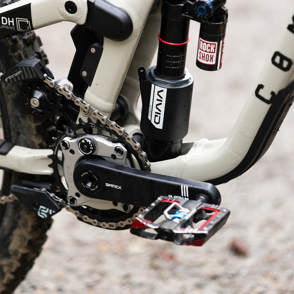 Close-up of a mountain bike's chain mechanism with visible brand logos on a blurred background.