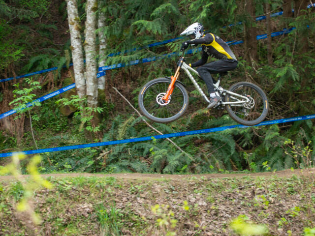 Person on a mountain bike in a forested area with blue ropes marking the course.