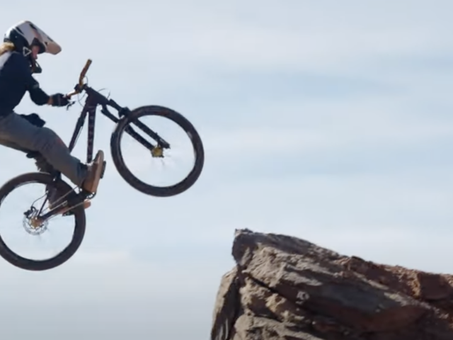 Person on a bicycle performing a stunt over a cliff with a clear sky background