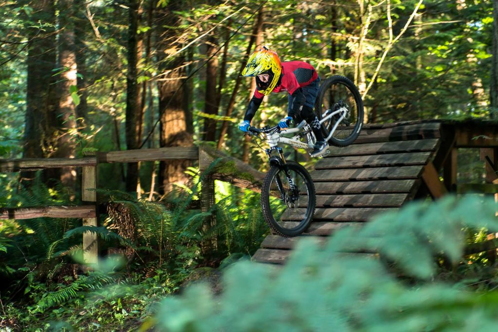 Person riding a mountain bike on a wooden ramp in a forest setting