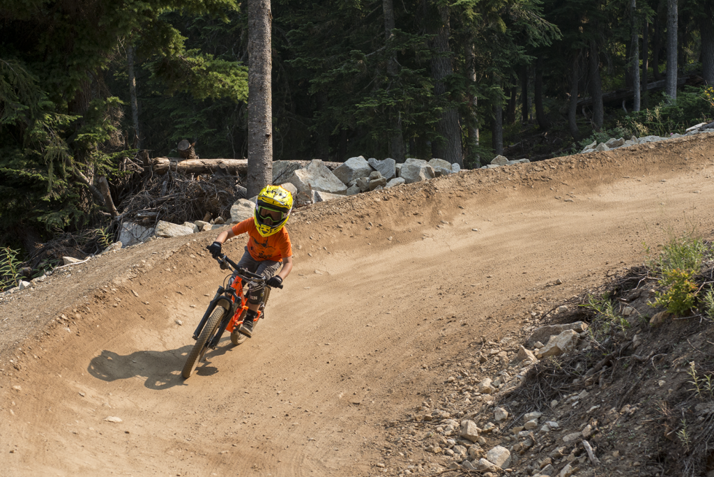Child riding a mountain bike on a dirt trail with trees in the background