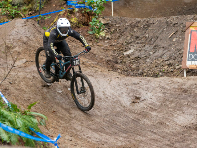 Biker in action on a dirt track with a helmet and protective gear.
