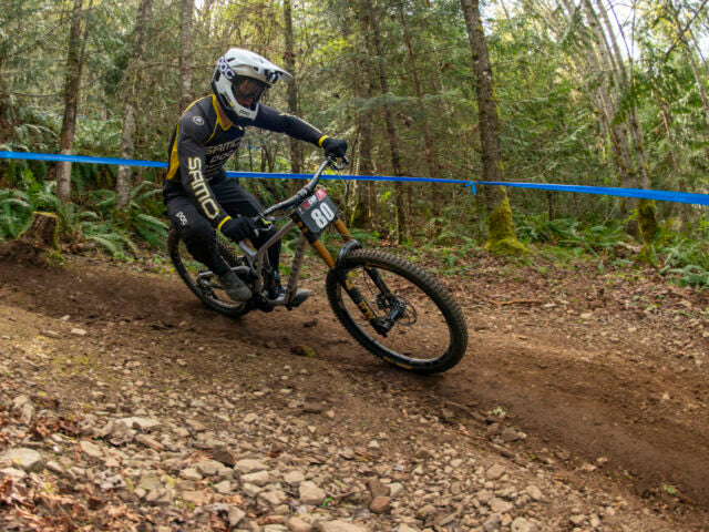 Biker racing downhill on a dirt track with trees in the background