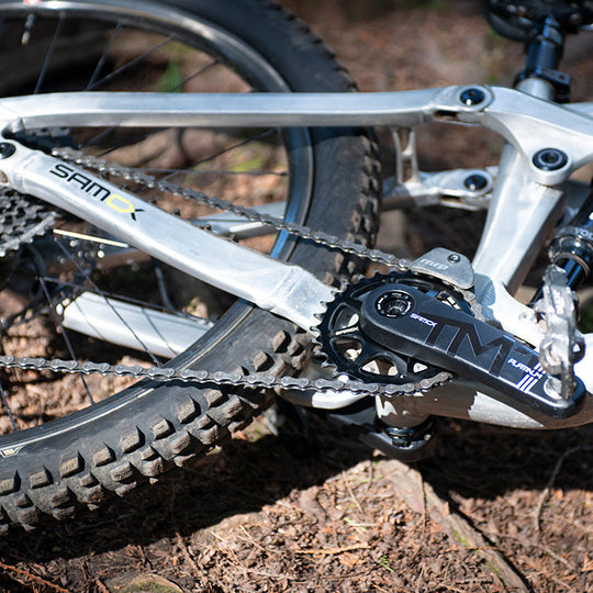 Close-up of a bicycle chain and gear system on a forest floor.